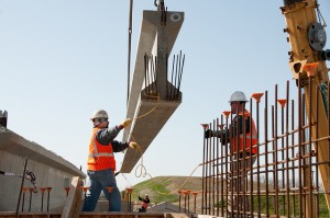 Two workers lower a cement girder into position
