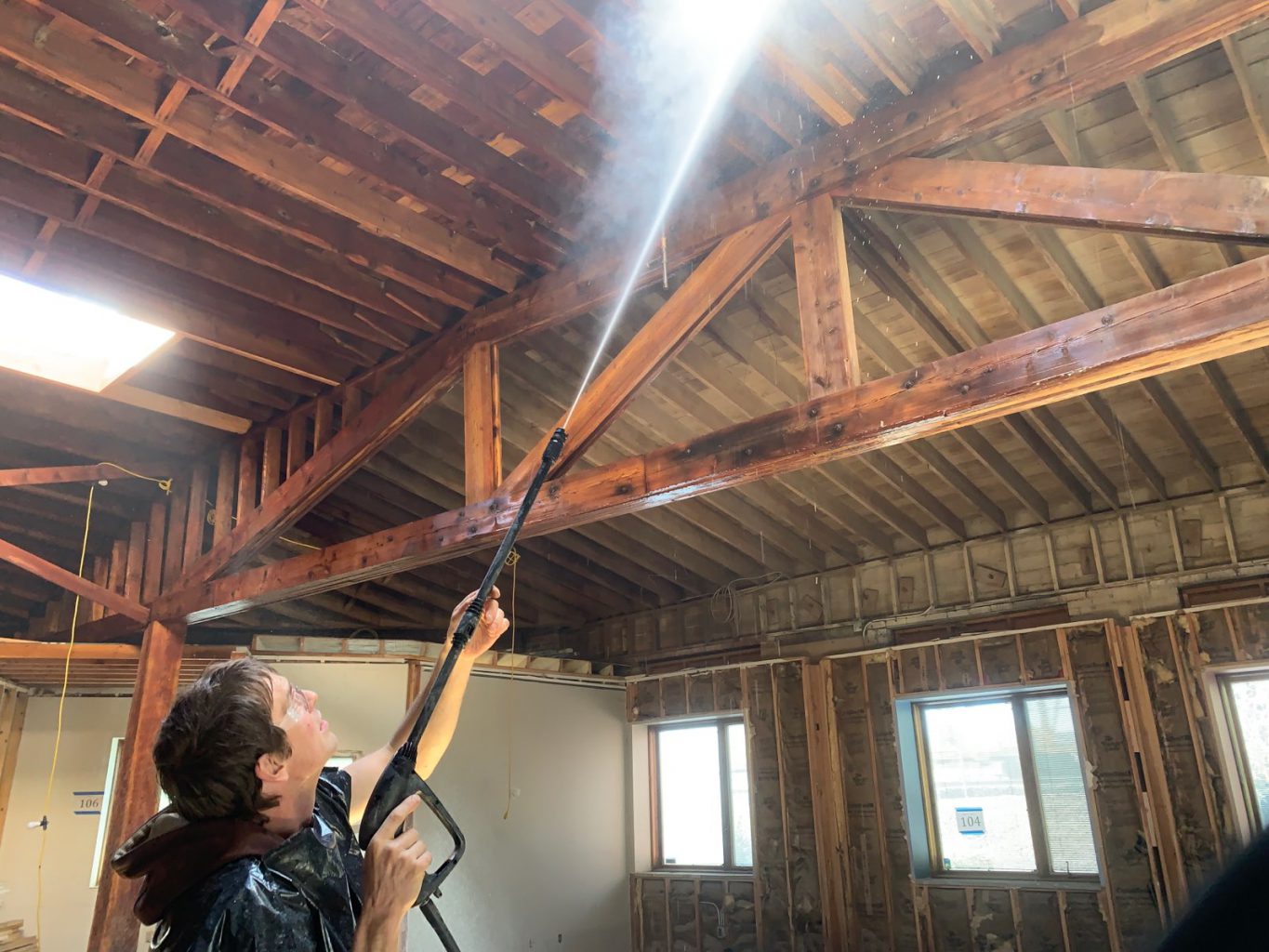Worker blasts ceiling with water to remove old paint from trusses and rafters